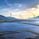 Stunning landscape featuring solar panels and wind turbines at sunrise, symbolizing sustainable energy.